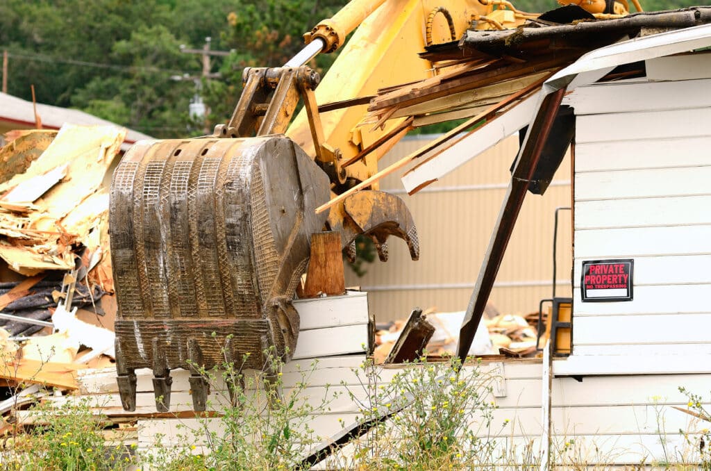 Excavator demolishing a house marked Private Property, with debris scattered around and a focus on construction machinery.
