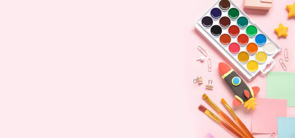 Depositphotos_667607602_XL Colorful art supplies on a pink background, including watercolor paints, paintbrushes, paper clips, and a clay rocket for creative projects. | Sky Rye Design Colorful art supplies on a pink background, including watercolor paints, paintbrushes, paper clips, and a clay rocket for creative projects.