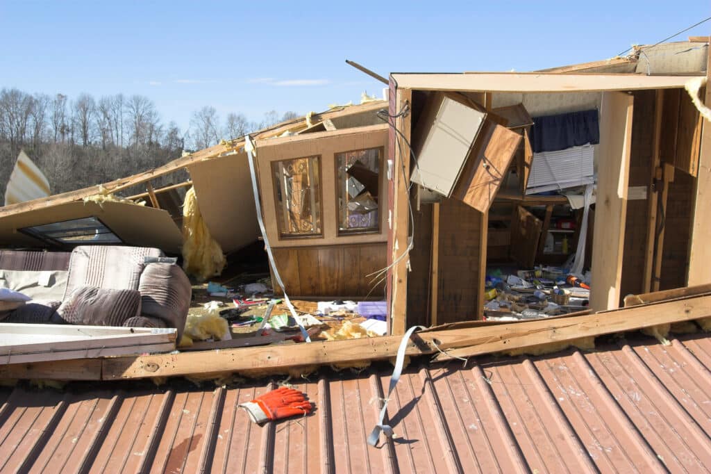 Collapsed house roof with debris after a severe storm, showcasing extensive property damage under blue sky.