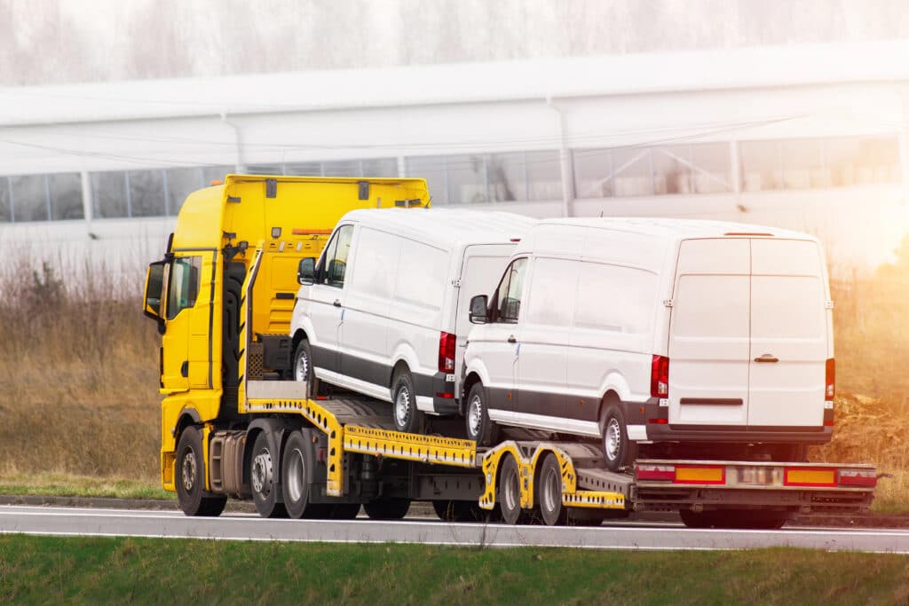 Yellow truck transporting white vans on a highway, showcasing automotive logistics and freight transportation on a clear day.