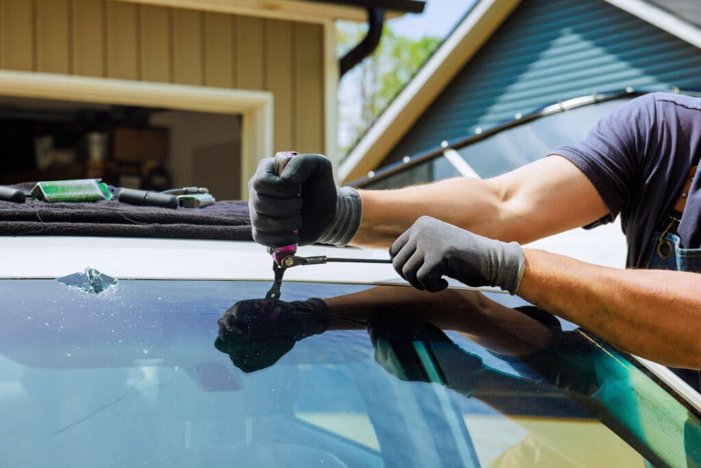 Technician repairing a cracked car windshield with tools in a workshop, emphasizing automotive glass repair and maintenance.