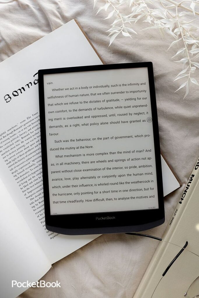 Digitallesen für alle Formate - PocketBook InkPad X Pro E-reader displaying text, placed on a bed with white leafy decor and open book. Ideal for reading enthusiasts and cozy settings. | Sky Rye Design E-reader displaying text, placed on a bed with white leafy decor and open book. Ideal for reading enthusiasts and cozy settings.