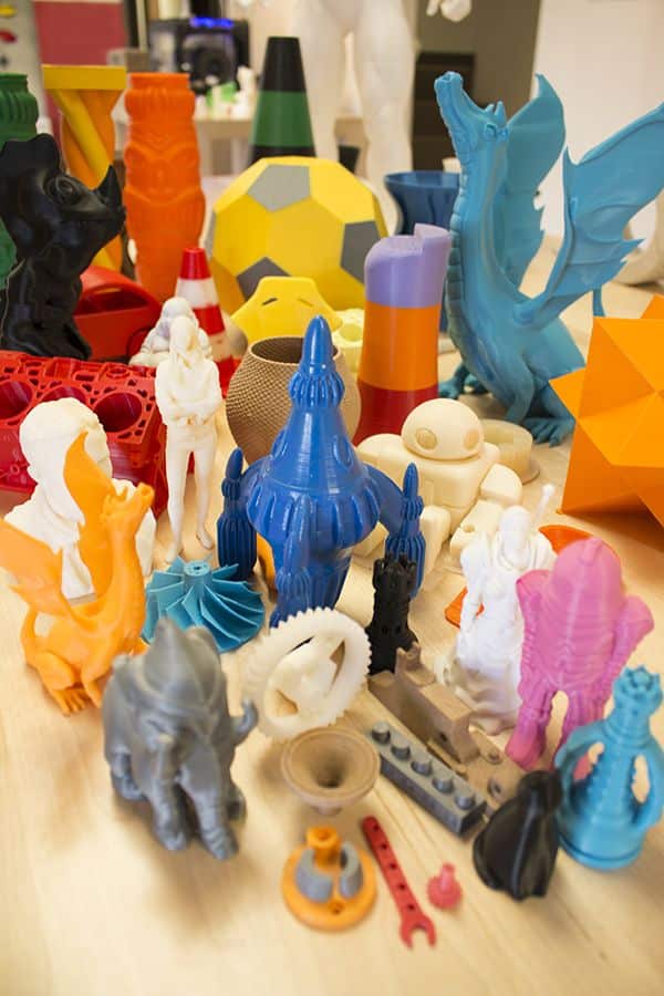 Colorful 3D printed objects including figurines, geometric shapes, and abstract designs arranged on a table in a creative display.