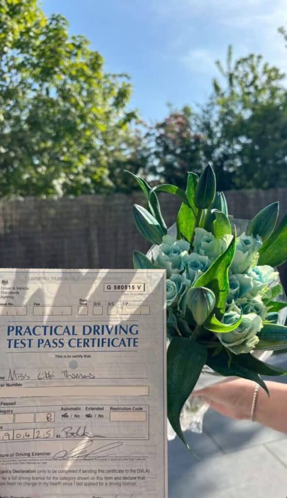 Driving test pass certificate and bouquet held outdoors under clear blue sky.