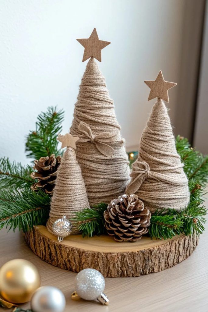 DIY Christmas trees wrapped in twine with star toppers, surrounded by pinecones and ornaments on a wooden base with greenery.