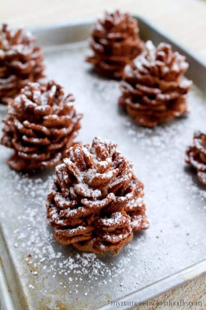 Edible Chocolate Pinecones _ Recipe by My Name Is Snickerdoodle Chocolate pinecone treats on a baking tray dusted with powdered sugar, perfect for festive occasions or holiday dessert inspiration. | Sky Rye Design Chocolate pinecone treats on a baking tray dusted with powdered sugar, perfect for festive occasions or holiday dessert inspiration.