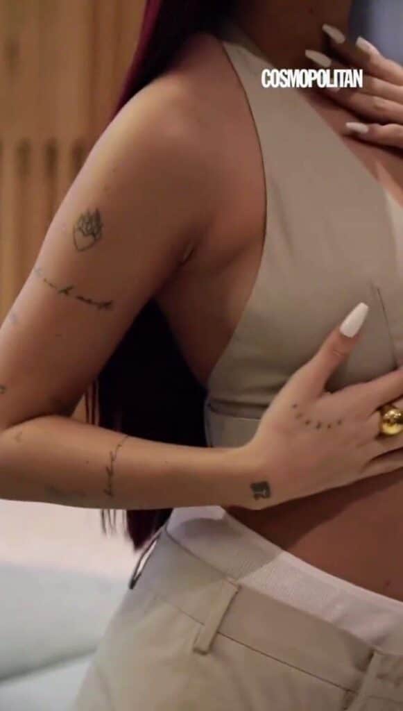 Emilia Close-up of a woman's torso with tattoos, wearing a beige top. She has long nails and holds her hand over her chest, showcasing rings. | Sky Rye Design Close-up of a woman's torso with tattoos, wearing a beige top. She has long nails and holds her hand over her chest, showcasing rings.