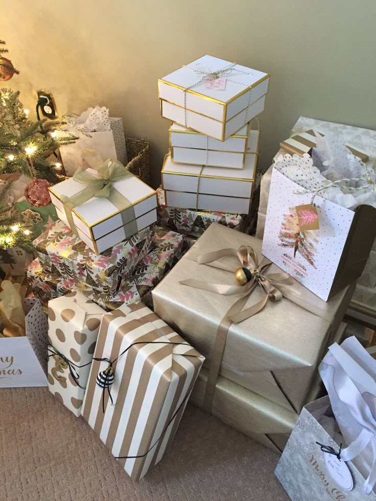 Christmas gifts wrapped in elegant paper with bows and ribbons, stacked under a decorated tree, creating a festive holiday atmosphere.