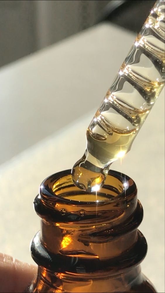 Close-up of a dropper with golden liquid poised above an amber glass bottle, reflecting light. Ideal for skincare or essential oils.