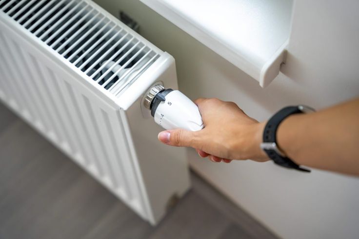 Hand adjusting radiator thermostat for optimal room temperature control. Home heating efficiency and comfort settings.