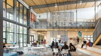 Modern university atrium with students studying and socializing in a bright, open space featuring high ceilings and large windows.