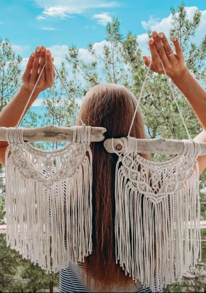 FBrsfgv Woman holding macramΓ© wall hangings with trees in the background under a blue sky. | Sky Rye Design Woman holding macramΓ© wall hangings with trees in the background under a blue sky.
