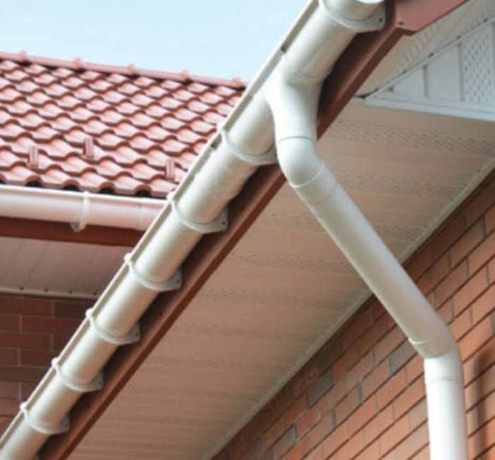 Close-up of a house roof with red tiles and white PVC gutters against a blue sky. Efficient rainwater drainage system.
