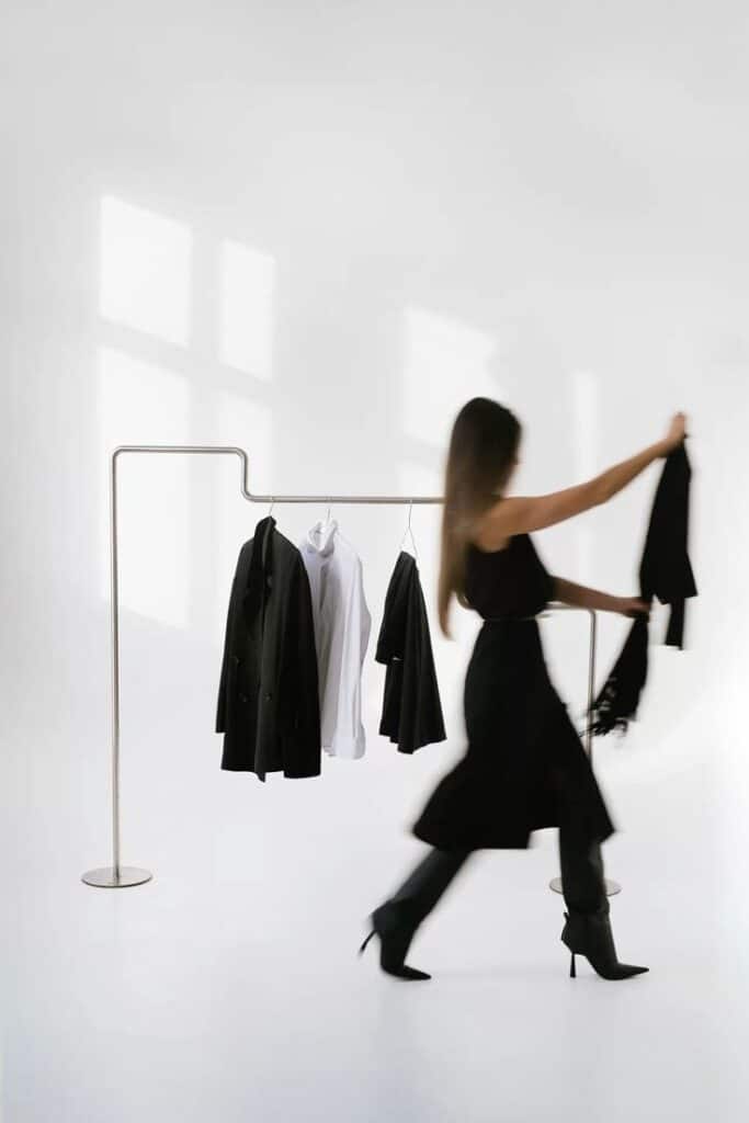 Woman walking past a clothing rack with black and white garments in a minimalist room.