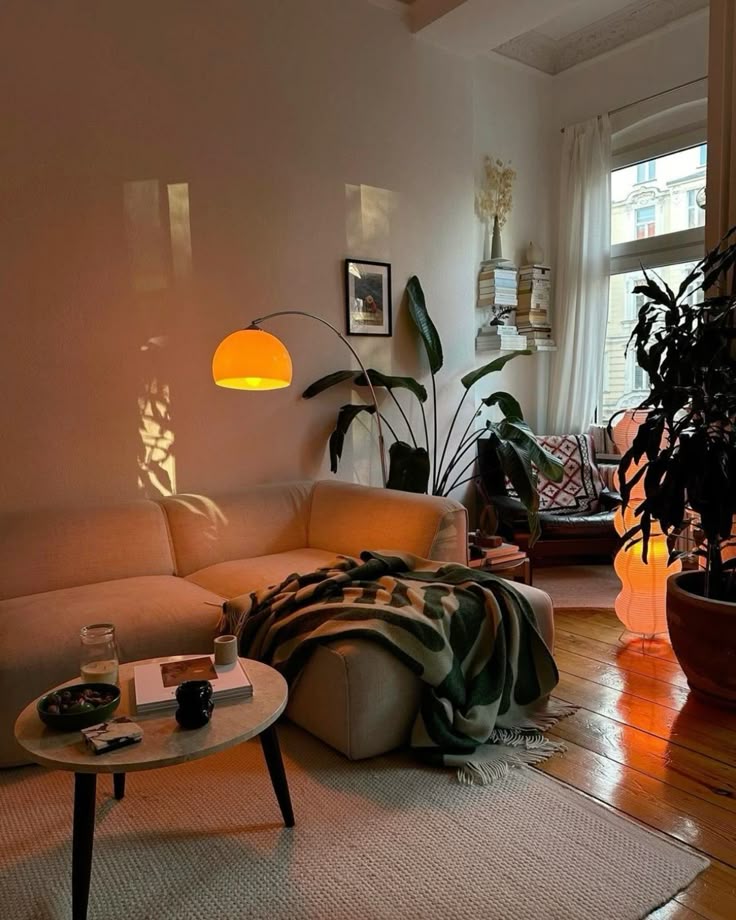 Cozy living room with a beige sofa, warm lighting, houseplants, and wooden floors, creating a relaxing and inviting atmosphere.