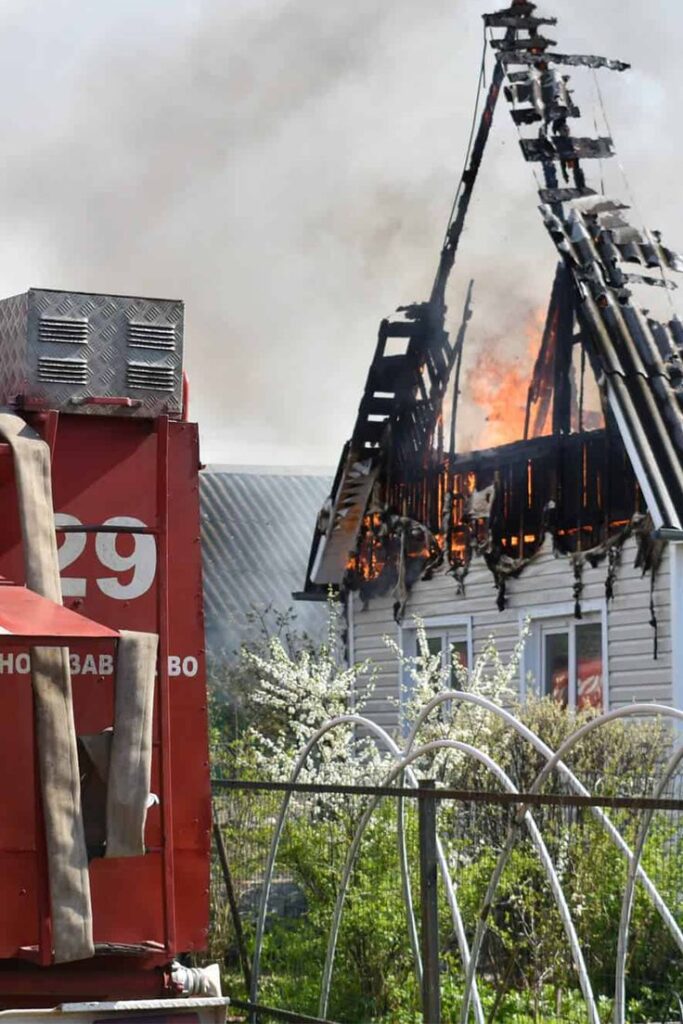Firetruck at the scene of a house fire, roof ablaze with smoke rising, highlighting emergency response.