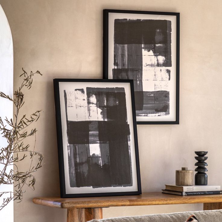 Black and white abstract art in frames on a wooden table next to stacked books and candles, enhancing a modern interior design.