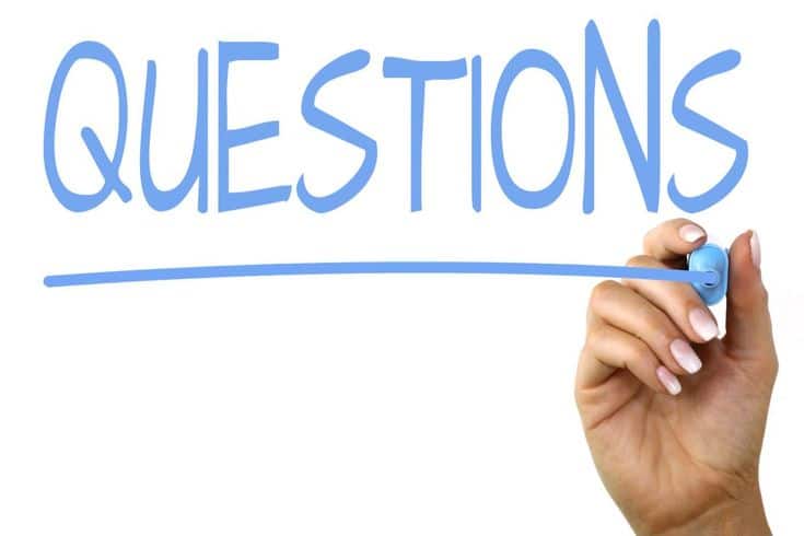 Hand writing 'questions' in blue marker on whiteboard, emphasizing inquiry and communication.