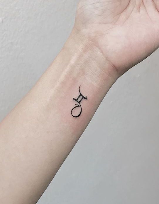 Minimalist Gemini symbol tattoo on a wrist, showcasing elegant black ink design on light skin, close-up view.
