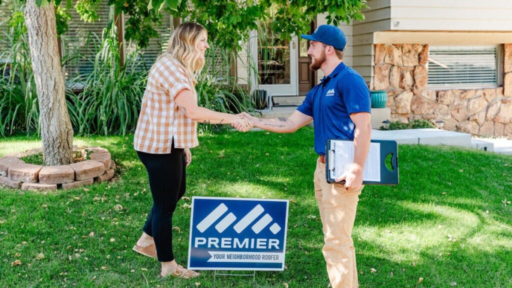 Roofer and homeowner shaking hands in front of house with Premier sign, symbolizing trust and partnership.