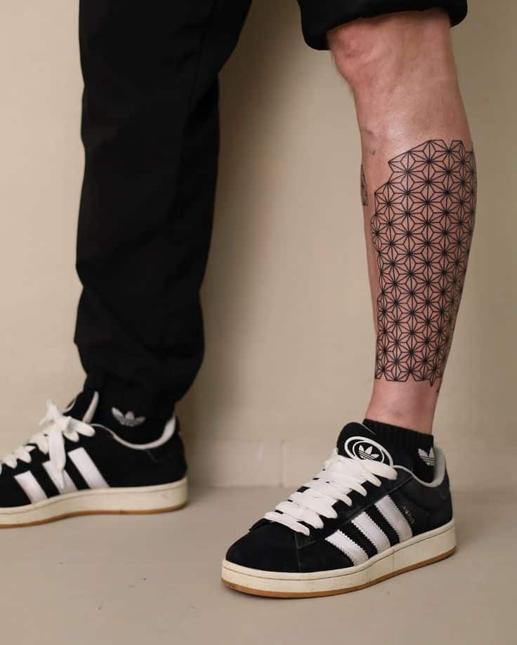 Geometric calf tattoo and Adidas sneakers with black joggers outfit.