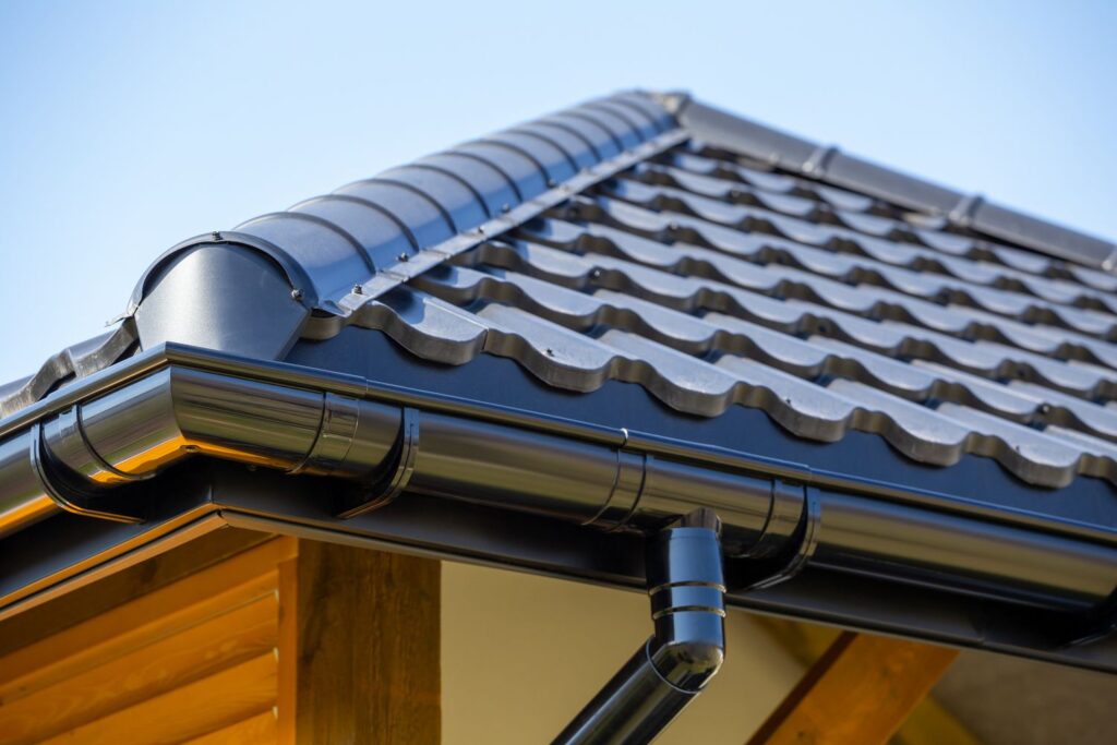 Modern tiled roof with black metal gutters against a clear blue sky, showcasing durable construction and weather protection.