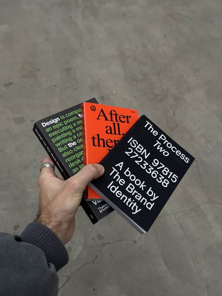 Hand holding three design books with vibrant covers and bold typography, showcasing creative branding and identity themes.