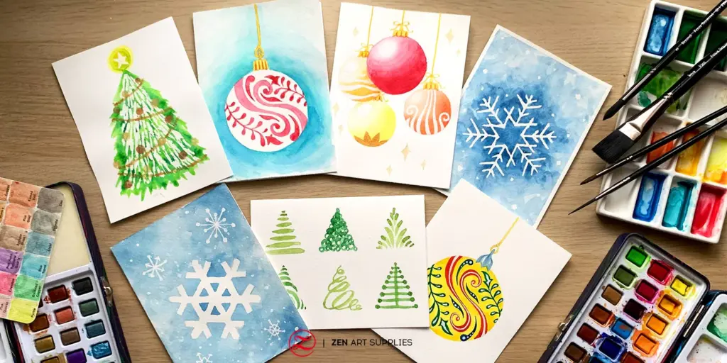 Watercolor Christmas cards featuring trees, ornaments, and snowflakes, surrounded by paint brushes and palettes on a wooden table.