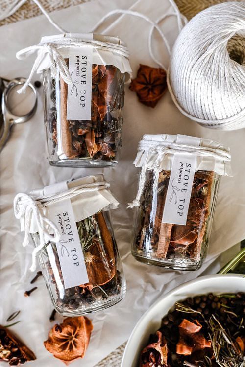 Jars of homemade stovetop potpourri with spices and herbs on rustic paper, surrounded by twine and scissors, creating a cozy ambience.