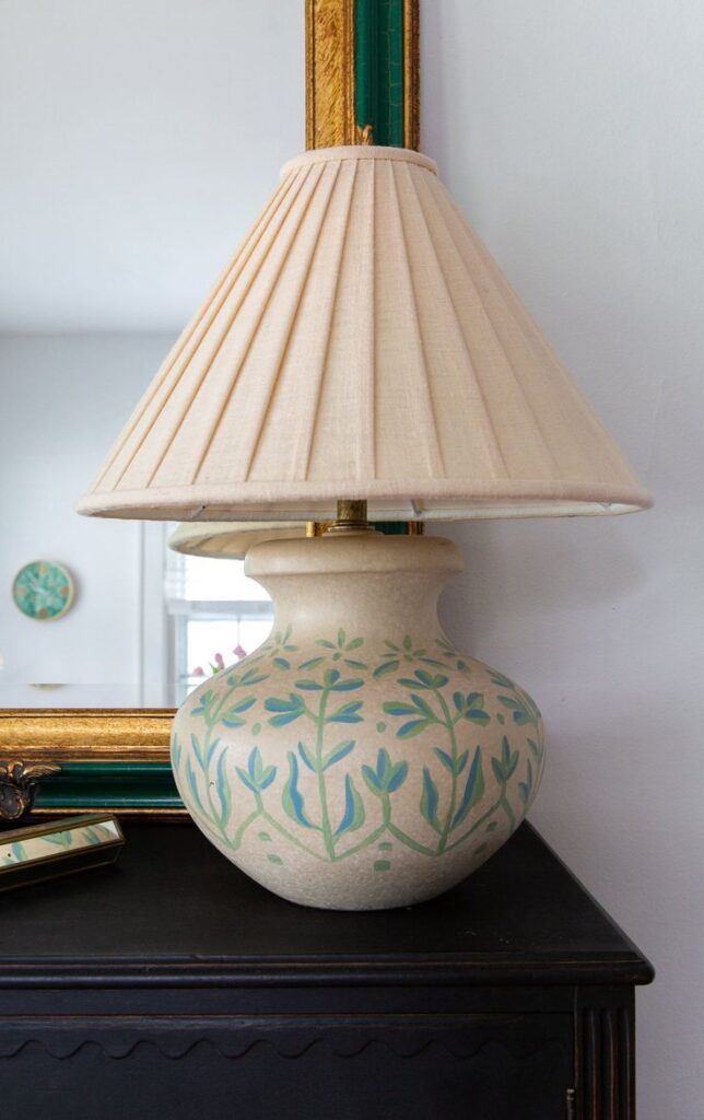 Ceramic table lamp with floral patterns and a beige pleated shade on a dark wooden surface, accenting a classic home decor style.