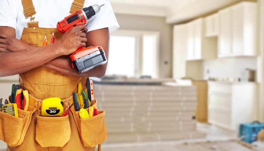 Builder in a tool belt holding a drill in a modern kitchen renovation setting.