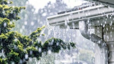 Rainwater overflows from a roof gutter during a heavy rainstorm, highlighting the need for proper drainage and maintenance.
