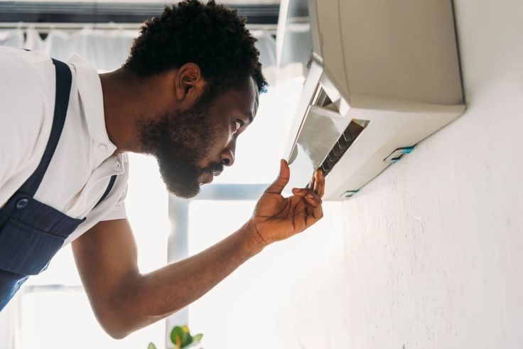 Technician inspecting wall-mounted air conditioner for maintenance, ensuring efficient cooling in a modern home environment.