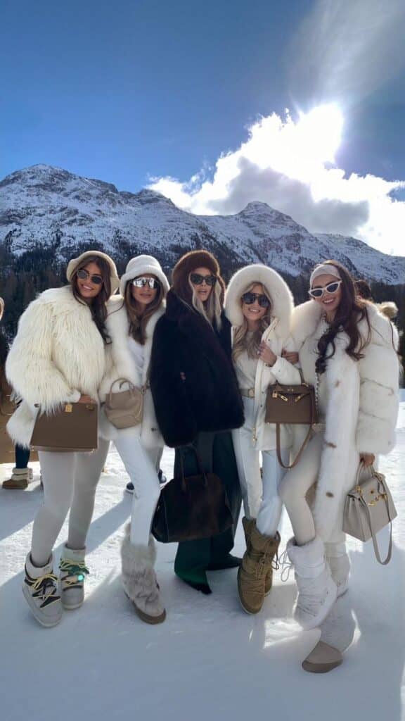Group of women in stylish winter outfits posing in snowy mountains under sunny skies.
