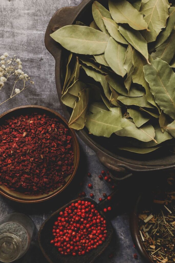 How to Make Homemade Potpourri + Winter Blend Recipe Assorted aromatic herbs and spices including bay leaves, dried red chilies, and red peppercorns in bowls on a rustic surface. | Sky Rye Design Assorted aromatic herbs and spices including bay leaves, dried red chilies, and red peppercorns in bowls on a rustic surface.