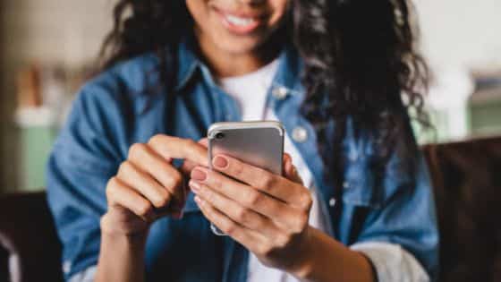 Woman Using Smartphone A woman with curly hair interacting with a smartphone while seated indoors. | Sky Rye Design A woman with curly hair interacting with a smartphone while seated indoors.