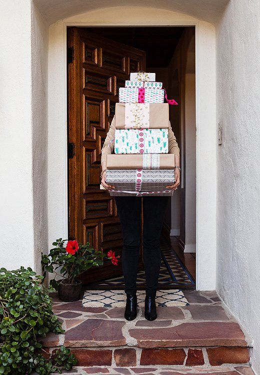How to Throw a Virtual Gift Exchange Person carrying a stack of wrapped gifts by a wooden door, surrounded by plants. Holiday spirit and celebration. | Sky Rye Design Person carrying a stack of wrapped gifts by a wooden door, surrounded by plants. Holiday spirit and celebration.