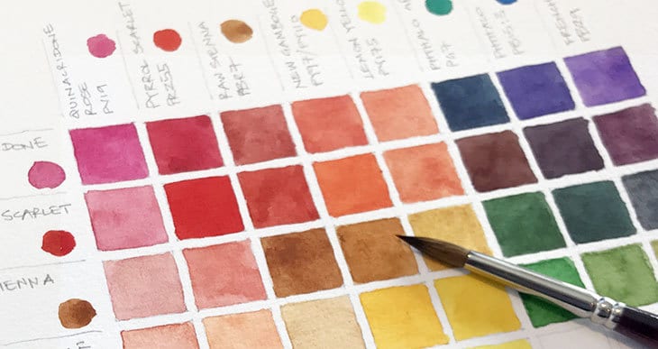 Watercolor paint swatches with brush on paper, showcasing a vibrant range of colors from shades of red, orange, blue, and yellow.
