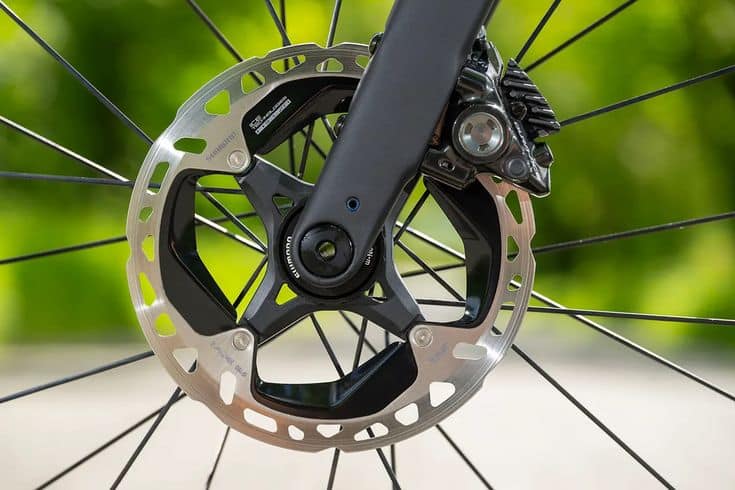 Close-up of a bike disc brake rotor and caliper showcasing precise engineering against a blurred green background. Ideal for cycling enthusiasts.