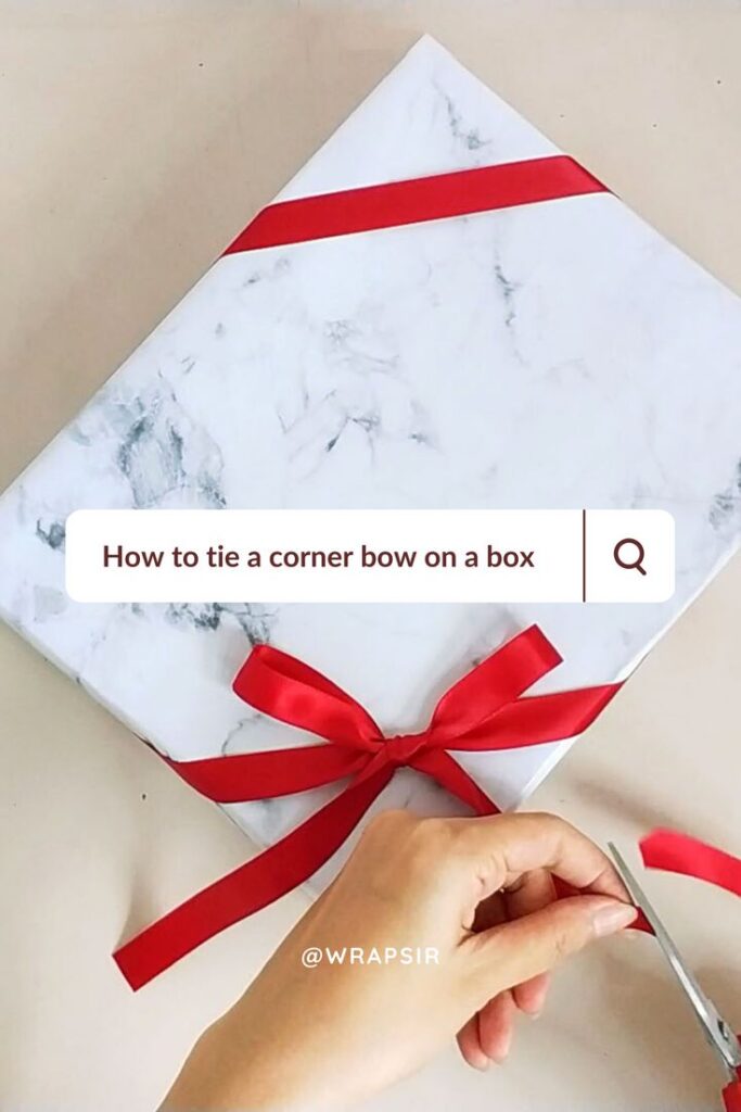 How to wrap diagonally ribbon _ ribbon on corners of present Gift box with marble wrapping, tied with a red corner bow. Hand trimming ribbon. Text overlay: How to tie a corner bow on a box. | Sky Rye Design Gift box with marble wrapping, tied with a red corner bow. Hand trimming ribbon. Text overlay: How to tie a corner bow on a box.