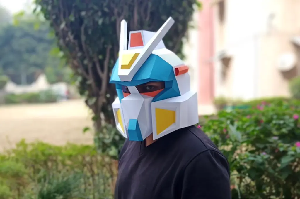 IMG__11 Person wearing a colorful, geometric robot helmet outdoors near trees. | Sky Rye Design Person wearing a colorful, geometric robot helmet outdoors near trees.