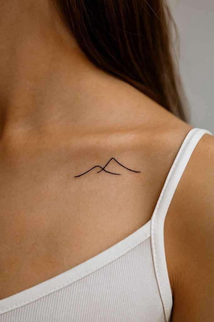 Ideas_tatto Minimalist mountain tattoo on a woman's upper chest, near her shoulder, wearing a white tank top. Simple and elegant design. | Sky Rye Design Minimalist mountain tattoo on a woman's upper chest, near her shoulder, wearing a white tank top. Simple and elegant design.