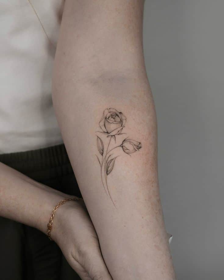 Minimalist rose tattoo on forearm with delicate line work, highlighting the elegance of the floral design.