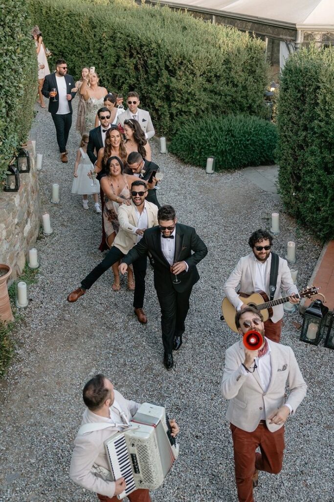 Italian Wedding Photography_ Music Laughter Guests joyfully parade at a wedding, led by musicians with an accordion and guitar. | Sky Rye Design Guests joyfully parade at a wedding, led by musicians with an accordion and guitar.