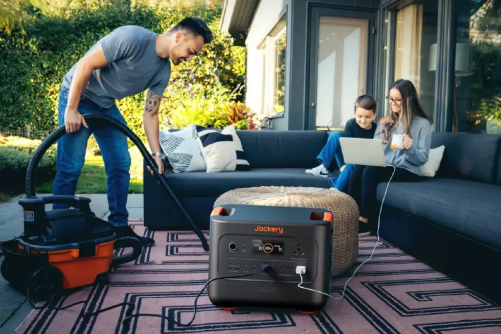 Jackery-Solar-Generator-HomePower-3000 Man vacuuming outside with a portable power station nearby; family enjoys laptop and drinks on the sofa. | Sky Rye Design Man vacuuming outside with a portable power station nearby; family enjoys laptop and drinks on the sofa.
