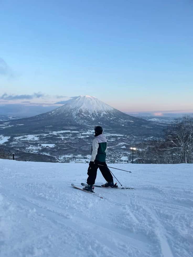 Person skiing on a snowy slope with Mount Yotei in the background, Niseko, Japan. Clear blue sky, perfect for winter sports.