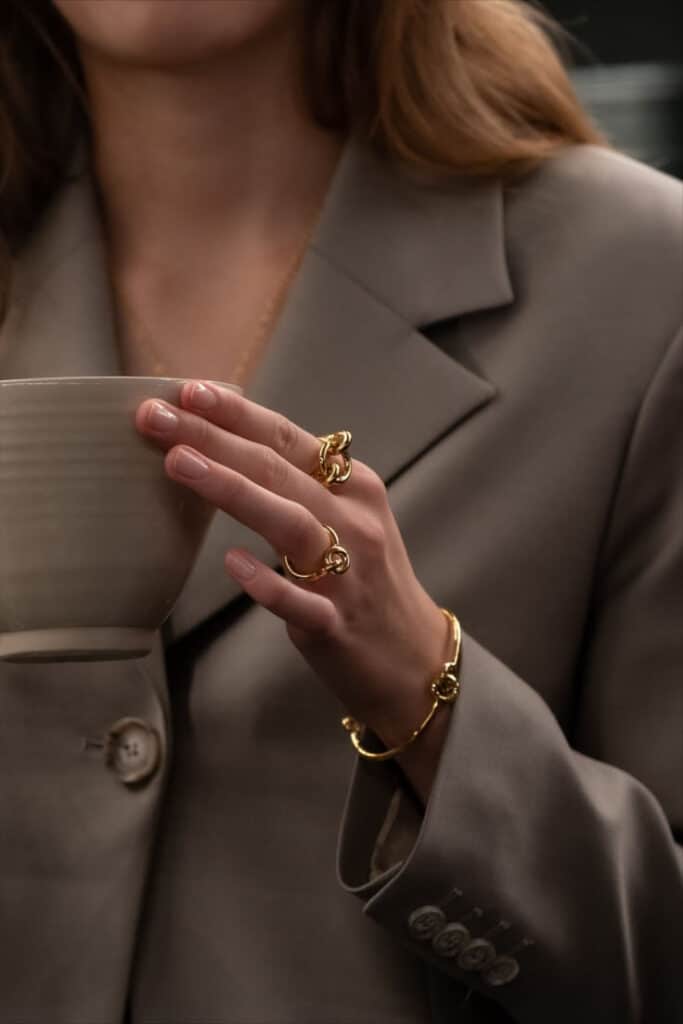 Lara Bohinc x Skultuna Woman in a suit holding a ceramic cup, wearing elegant gold rings and bracelet. | Sky Rye Design Woman in a suit holding a ceramic cup, wearing elegant gold rings and bracelet.