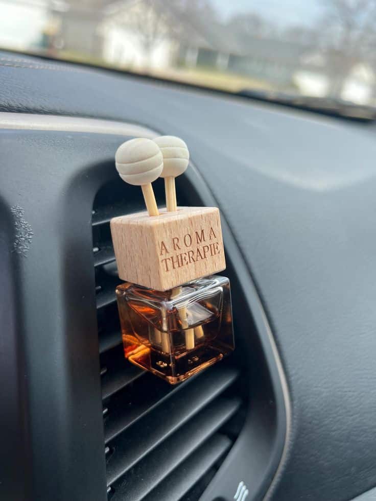 Car vent aromatherapy diffuser with wooden top and amber glass, enhancing the interior with a refreshing scent.
