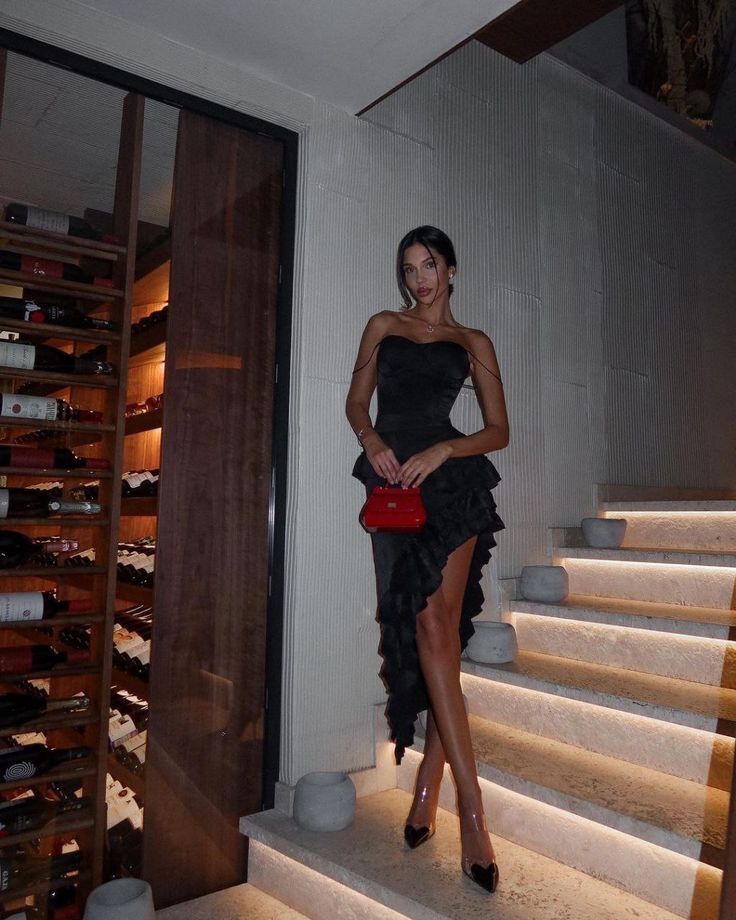 Level up get back on your ex_ Elegant woman in a black evening dress with a red purse, standing by a wine cellar on illuminated stairs. | Sky Rye Design Elegant woman in a black evening dress with a red purse, standing by a wine cellar on illuminated stairs.