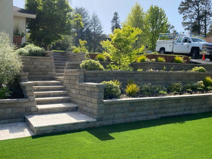 Terraced garden with stone steps, lush greenery, and parked truck under blue sky, creating a serene outdoor landscape setting.